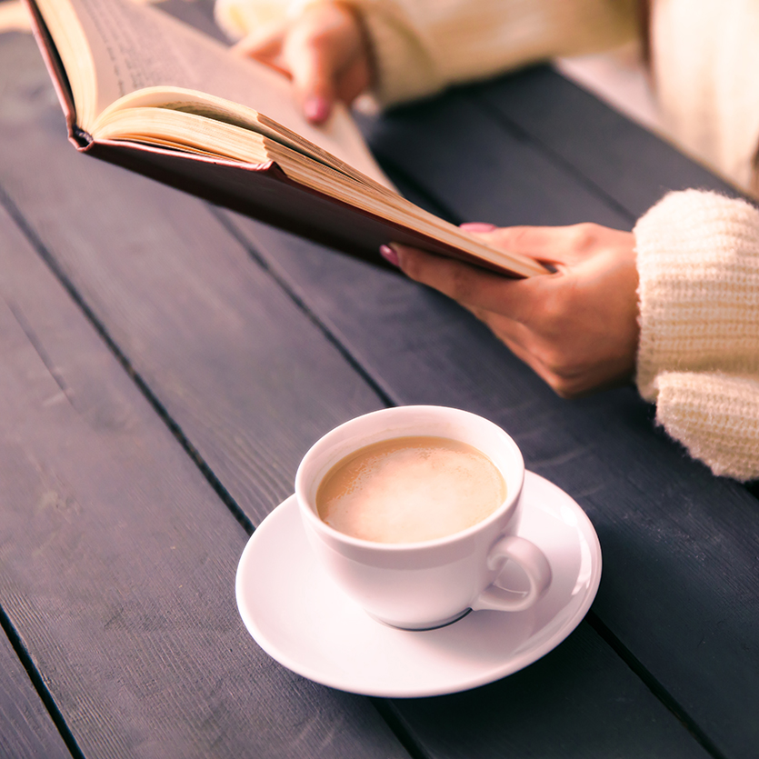 Frau lesend am Tisch mit einer Tasse Kaffee